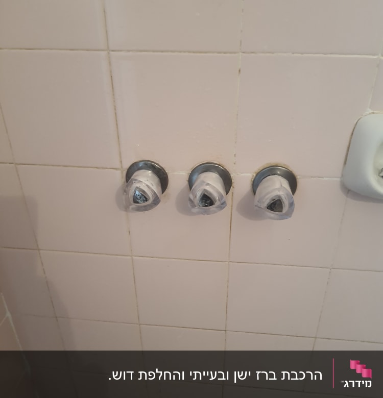 שלושה ברזים על קיר אריחים בחדר אמבטיה